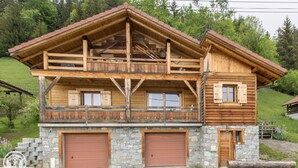 Un chalet en bois à deux étages, doté de fondations en pierre, de grandes portes de garage et d’un balcon.