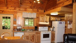 A wooden cabin kitchen with a dining area, a refrigerator, a stove, and wooden cabinets. -  Cherokee Family Cabin  (Hico)