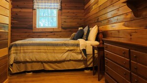 A wooden cabin bedroom with a bed, a nightstand, a dresser, a window with blinds, and a ceiling fan. -  Cherokee Family Cabin  (Hico)