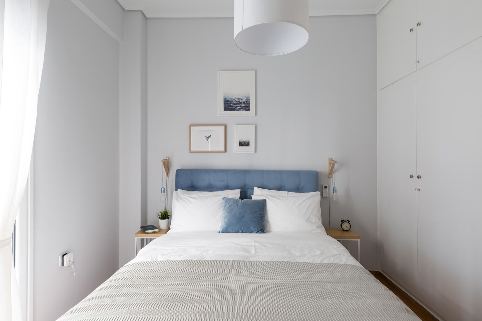 Et soveværelse med seng, natborde, sengetøj, lampe på væggen og billeder i rammer.