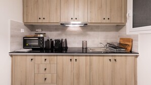 Een kleine keuken met houten kastjes, een inbouwmagnetron, een waterkoker en een koffiezetapparaat.
