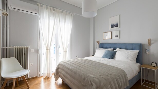 Een slaapkamer met een bed, een stoel, een nachtkastje en een raam met gordijnen.