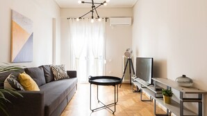 Een moderne woonkamer met een grijze bank, een ronde zwarte tafel, een tv op een meubelstuk en een plafondlamp.
