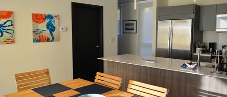 A modern kitchen with a built-in refrigerator, wooden dining table with chairs, and two wall-mounted paintings.