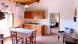A kitchen with wooden cabinets, a dining table with chairs, and a view into a bedroom. - Montegonfoli 6 San Gimignano Countryside Apt. with amazing views and pool (san gimignano)