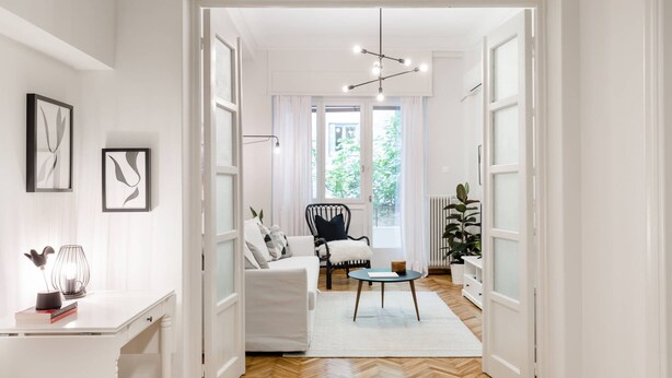 A bright hallway with a white door leading to a living room with a sofa, a black chair, and a small table. - Classy & Charming 1BD Apartment in Kolonaki (Athens)