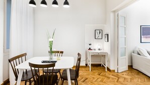 A dining area with a white table, four chairs, and a vase with flowers. There is a white desk with a lamp and a framed picture on the wall. - Classy & Charming 1BD Apartment in Kolonaki (Athens)
