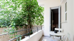 A balcony with a stone wall, a metal railing, a small table with a cushion, and a door leading to an interior room. - Classy & Charming 1BD Apartment in Kolonaki (Athens)