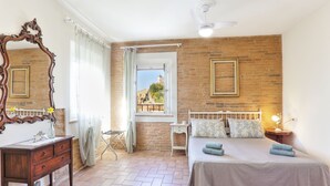 A bedroom with a brick wall, a large mirror, a bed with pillows, a nightstand, and a window with a view. - Two-room apartment on 2 levels of 48 m2 (palaia)