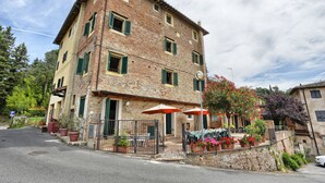 A two-story building with a brick facade, green shutters, and outdoor seating with umbrellas. - Two-room apartment on 2 levels of 48 m2 (palaia)
