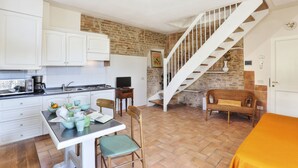 A kitchen with white cabinets, a dining table with chairs, a staircase, and a wicker chair. - Two-room apartment on 2 levels of 48 m2 (palaia)