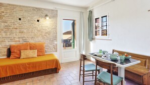 A room with a brick wall, a bed with orange bedding, a dining table with chairs, and a view through a door. - Two-room apartment on 2 levels of 48 m2 (palaia)