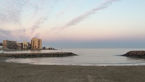 Un paysage côtier avec une plage de sable, une mer calme et une rangée d’immeubles à plusieurs étages en arrière-plan.