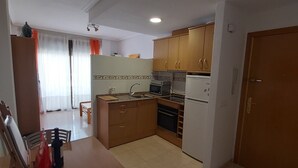 Une cuisine de taille réduite avec des meubles de rangement en bois, une table à manger avec des chaises et un réfrigérateur.