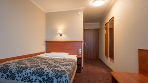 A hotel room with a bed, a nightstand, a lamp, a wooden headboard, and a mirror on the wall. - Hotel Krakus (Kraków)