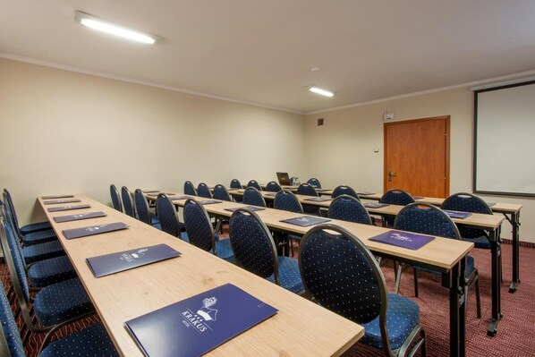 A conference room with long tables, blue chairs, and a projector screen. - Hotel Krakus (Kraków)