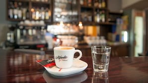 A bar setting with a cup of coffee labeled 'Alfredo' and a glass of water on a wooden table. - Hotel Krakus (Kraków)