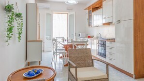 Una cocina moderna con armarios blancos, una zona de comedor con sillas de mimbre y una planta colgante.