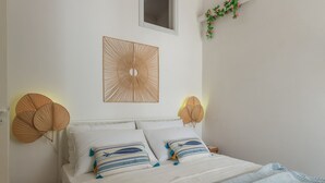 Una cama con ropa blanca y almohadas a rayas, un panel decorativo montado en la pared y dos lámparas fijadas a la pared.