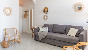 Una sala de estar con un sofá gris, sillas de mimbre, una mesita con velas y espejos decorativos en las paredes.