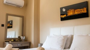 Een hotelkamer met een bed, nachtkastje, spiegel, een wandairconditioner en een schilderij van een gebouw.