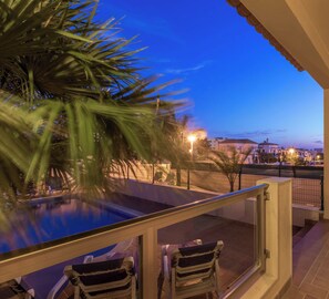 Un balcón con piscina, sillas y vistas a edificios al atardecer.