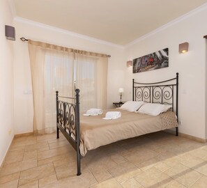 Habitación de hotel limpia y segura con cama, ventana con cortinas, un cuadro en la pared y balcón con puerta de vidrio.