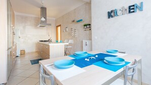 Een moderne keuken met een eetgedeelte, met een keukeneiland, witte kasten en een blauwe tafelkleed.