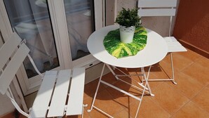 Een klein terras met een ronde tafel, twee witte stoelen en een bloempot.