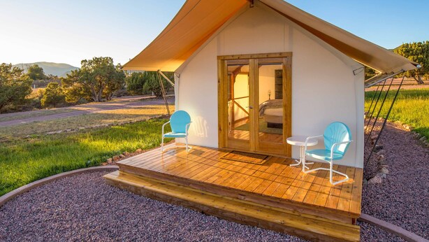 A small, single-story building with a sloped roof, a wooden deck, and two blue chairs. - Glamping Tent Single Queen - Royal Gorge Cabins (Cañon City)