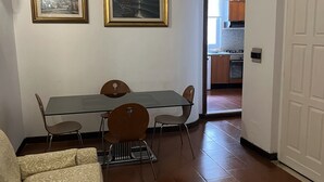 Un comedor con mesa y sillas de vidrio, un sofá y dos cuadros en la pared.