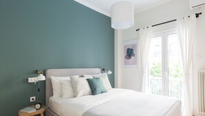 Quarto com cama, mesa de cabeceira, abajur e vista para o exterior.