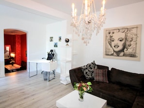 Un salon moderne avec un bureau blanc, un canapé marron foncé, un lustre et un grand portrait accroché au mur.