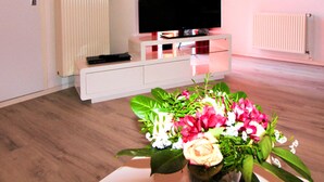 Un salon moderne avec un téléviseur à écran plat posé sur un meuble blanc, un radiateur et un plancher en bois.