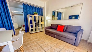 Uma sala de estar com um sofá cinzento, um rack branco para a TV e um espaço de jantar com mesa e cadeiras.