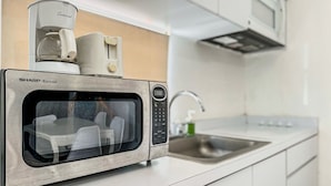 Cozinha moderna com micro-ondas embutido, máquina de café e coifa de aço inoxidável.