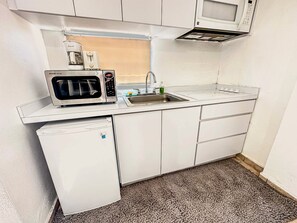 Eine kompakte Küchenzeile mit Mikrowelle, Kaffeemaschine, Spüle und kleinem Kühlschrank.