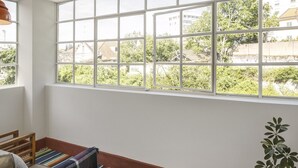 Ein Zimmer mit großem Fenster, einer Holzbank, einem farbenfrohen Teppich und einem Blumentopf.