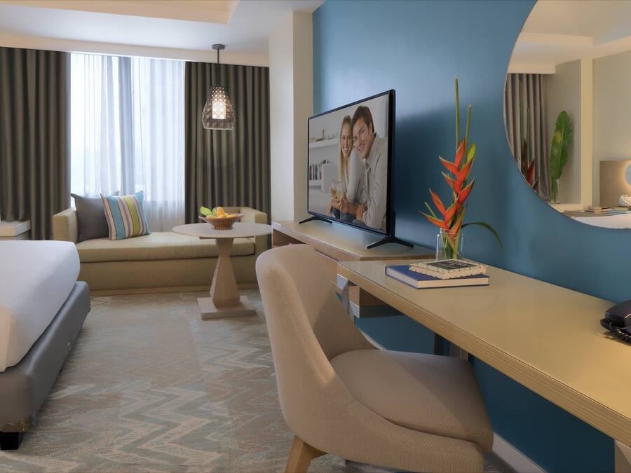 Een hotelkamer met een bed, een bureau met een computer, een stoel, een kleine tafel en een plant.