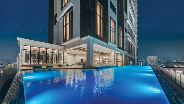 Un hotel moderno con piscina infinita en la azotea, amplias ventanas y vistas a la ciudad de noche.