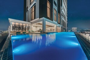 Un hotel moderno con piscina infinita en la azotea, amplias ventanas y vistas a la ciudad de noche.