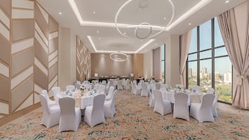 A banquet hall with round tables, white chairs, and a large window with a city view.