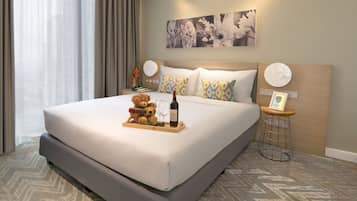 A hotel room with a large bed, a bedside table with a lamp, a teddy bear, a wine bottle, and a framed picture.