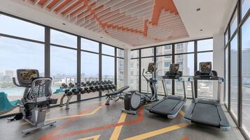 Ein Fitnessstudio mit Laufbändern, Crosstrainern und einer Hantelbank.