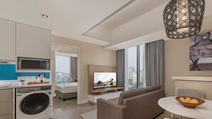 Una habitación de hotel moderna con kitchenette, lavadora, sofá, televisor y zona de comedor.