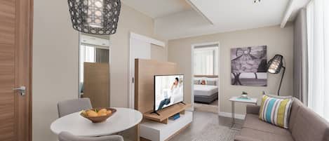 A modern living room with a TV on a wooden stand, a dining table with chairs, a sofa, and a decorative wall piece.