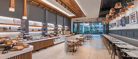 A modern cafe with wooden accents, a long counter with food displays, and a view of greenery outside.