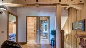 Un couloir intérieur en bois, avec un lit, une plante en pot et un escalier menant à une autre pièce.