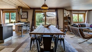 Un vaste espace dédié à la salle à manger, avec une longue table en bois, des chaises modernes et un luminaire suspendu.