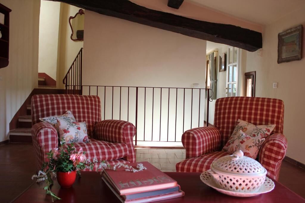 Een kamer met geruite fauteuils, een tafel met boeken en een bloevas, en een trap op de achtergrond.